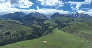 Yüksek karlı dağların eteklerindeki yeşil yuvarlanan tepeleri ve tarlaları süpürüyor.