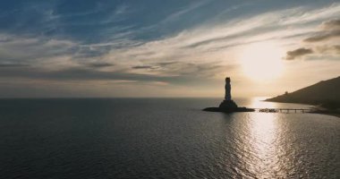 Gün batımında kayalık adada duran deniz feneri.