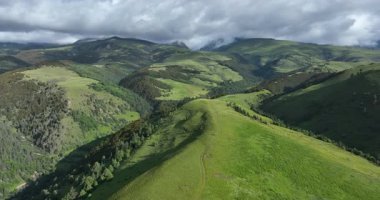 Bereketli, yeşil dağ yamaçları ve bulutlu bir gökyüzünün altındaki ağaç sırtlarıyla çevrili derin bir vadinin havadan görünüşü..