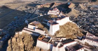 Hava manzarası, kayalık bir yamaçta inşa edilmiş beyaz duvarları ve kırmızı çatıları olan geleneksel bir Tibet kalesi veya manastırı gösteriyor..