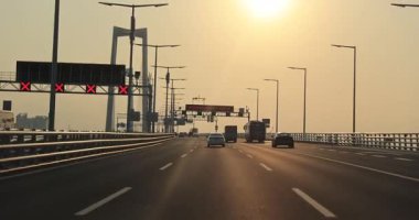 Modern bir kablodan geçen bir otoyol sisli bir gökyüzünün altındaki büyük kulelere uzanan bir köprü vazifesi görüyor..