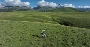 Dağ motorcuları çim tarlasına yavaş çekimde binerler. Uçsuz bucaksız yeşil çayırlar kayan tepelere ve berrak mavi gökyüzünün altındaki bulutlu dağlara doğru uzanır.. 