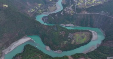 Koyu yeşil, dağlık vadide kıvrılan parlak turkuaz bir nehrin havadan görünüşü..