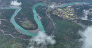 Koyu yeşil, dağlık vadide kıvrılan parlak turkuaz bir nehrin havadan görünüşü..