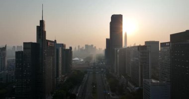 Yoğun bir şehir silueti ve merkez yol üzerinde puslu, sıcak gün batımı ya da gün doğumu manzarası. Çin