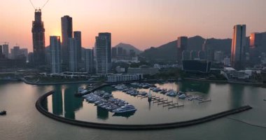 Günbatımı manzarası, şehir silüeti ve dağlarla desteklenen yatlarla dolu modern bir marina üzerinde..