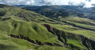 Dağların yeşil manzarası. Mavi gökyüzünün altındaki tepeler bulutlarla 
