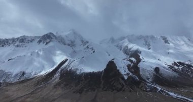 Karanlık, kayalık dağlar karla kaplı kasvetli, bulutlu ve sisli bir gökyüzünün altında.