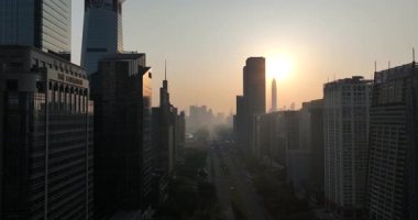 Gün doğumunda sisli, güneşli gökdelenler arasında uzanan geniş bir yol var..