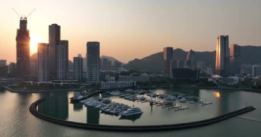 Günbatımı manzarası, şehir silüeti ve dağlarla desteklenen yatlarla dolu modern bir marina üzerinde..