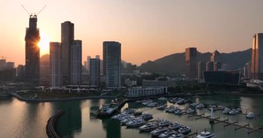 Günbatımı manzarası, şehir silüeti ve dağlarla desteklenen yatlarla dolu modern bir marina üzerinde..