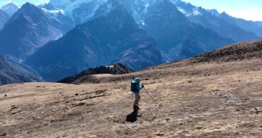 Büyük bir sırt çantası ve yürüyüş direğiyle yüksek irtifada, çorak bir arazide yürüyen bir yürüyüşçü..