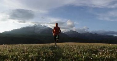 Arka planda karla kaplı bir dağ ile tepede koşan bir kişinin silueti. .