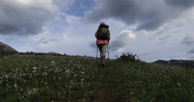 Yürüyüşçü dramatik bulutlu bir gökyüzünün altında çimenli bir dağ yamacına yükseliyor..