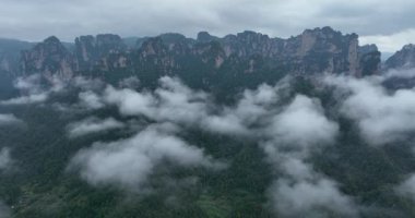 Sarp kumtaşı sütunlar ve tepeler bulutlu bir gökyüzünün altında yoğun yeşil bir ormanın üzerinde yükseliyor..