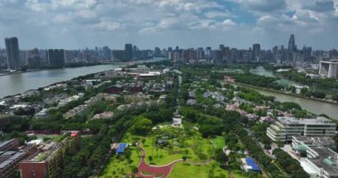 Modern Guangzhou siluetinin önünde yeşil bir park ve nehir görünüyor..