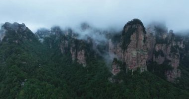 Kayalık tepeleri olan yemyeşil dağlar sislerle ve alçak bulutlarla örtülüdür..