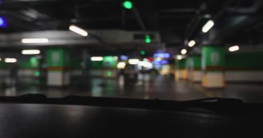 Gösterge panelinin bulanık görüntüsü, parlak yeşil ve kırmızı ışıkları olan karanlık, yeraltı otoparkını gösteriyor..