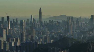 Gökdelenler, yüksek kuleler ve mavi bir alacakaranlık altında dağlar içeren yoğun şehir manzarası.