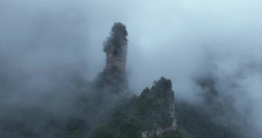 Sis ve alçak bulutlar sarp, dramatik, ormanla kaplı dağlar.