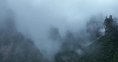 Sis ve alçak bulutlar sarp, dramatik, ormanla kaplı dağlar.