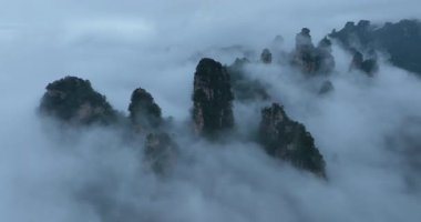Katıksız kaya sütunları ve dağ zirveleri yoğun sis ve bulutların üzerinde dramatik bir şekilde yükselir..