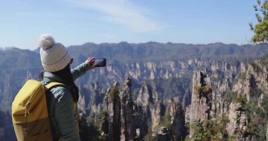 Dişi turist, dağlarda akıllı telefon yürüyüşü yaparak selfie çekiyor.