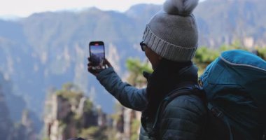 Dişi turist, dağlarda akıllı telefon yürüyüşü yaparak selfie çekiyor.