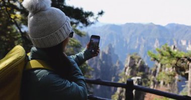 Dişi turist, dağlarda akıllı telefon yürüyüşü yaparak selfie çekiyor.