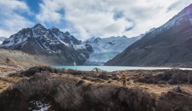 Sırt çantalı bir kadın yüksek irtifada asılı buzulun etrafında yürüyüş yapıyor.