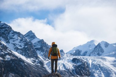 Sırt çantalı bir kadın yüksek irtifada asılı buzulun etrafında yürüyüş yapıyor.