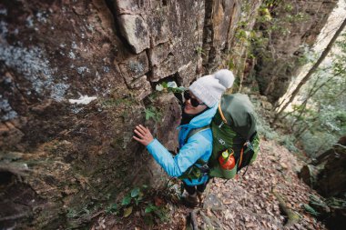 Sırt çantalı bir kadın dik orman patikasında yürüyüş yapıyor.