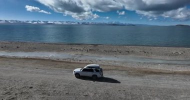 Yüksek irtifada göl kenarında çalışan off-road aracının hava görüntüleri.