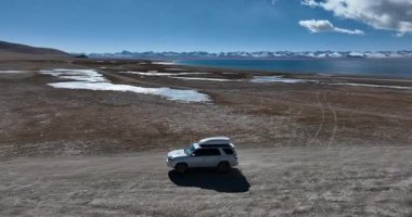 Yüksek irtifada göl kenarında çalışan off-road aracının hava görüntüleri.