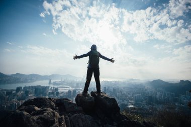 Başarılı kadın yürüyüşçü uçurumun kenarında duruyor kollarını uzatarak güzel Hong Kong 'a doğru.