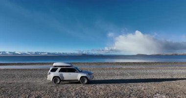 Sakin mavi gölün yakınına park edilmiş beyaz bir SUV.