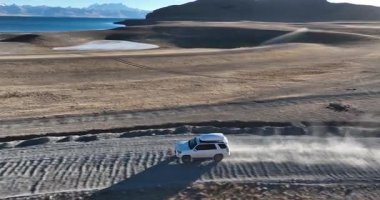 Toprak yolda giden beyaz bir cip.