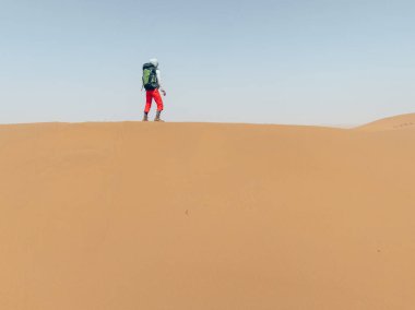 Yürüyüşçü kumlu çöl manzarasında yürüyor.