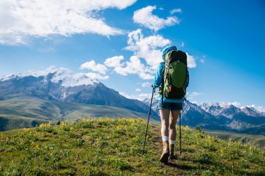 Yürüyüşçü mavi gökyüzünün altında dağlara doğru yürüyor.