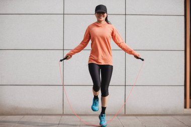 Dışarıda atletizm kıyafetleriyle ip atlayan bir kadın.