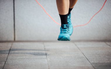 Mavi spor ayakkabılarıyla ip atlayan biri.