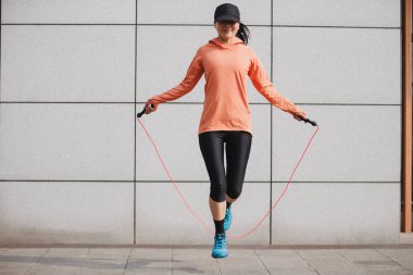 Dışarıda atletizm kıyafetleriyle ip atlayan bir kadın.