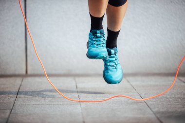 Mavi spor ayakkabı giyen biri ip atlıyor.