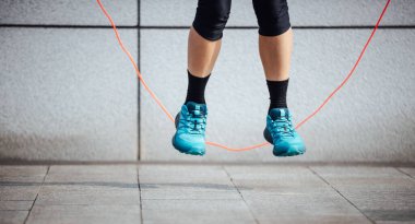 Mavi spor ayakkabı giyen biri ip atlıyor.