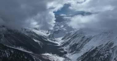Bulutlu gökyüzünün altındaki karlı dağ vadisi