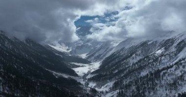 Bulutlu gökyüzünün altındaki karlı dağlar vadiyle