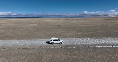 Uçsuz bucaksız bir arazide araba sürüyor.