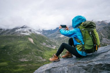 Yürüyüş yapan kadın, yüksek irtifada telefonuyla fotoğraf çekiyor.
