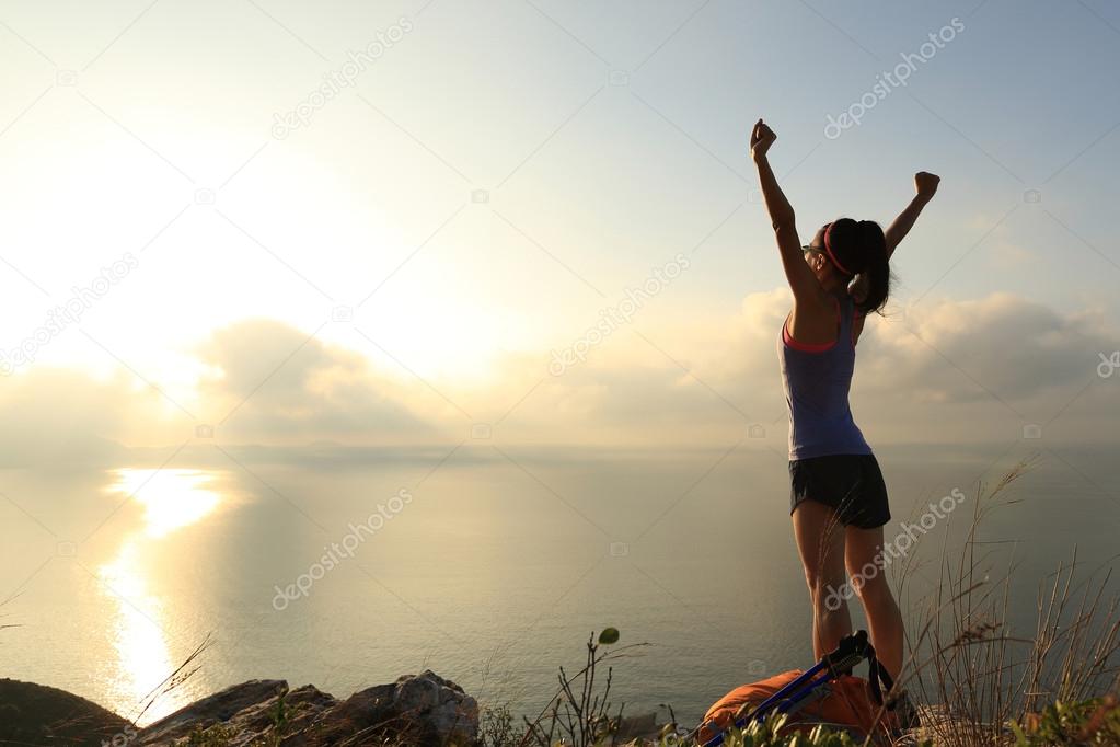 cheering young woman at mountain peak