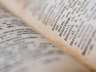 Üzerinde beyaz sayfalar ve siyah harfler olan bulanık arkaplan üzerine açık eski bir kitap.